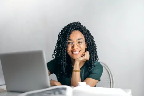 Black woman with glasses smiles with a laptop on her desk